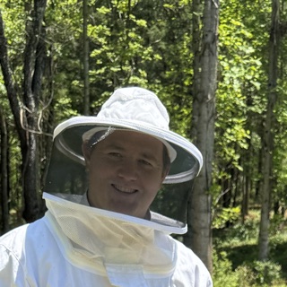 David, in a bee veil, smiling, with the woods behind him.